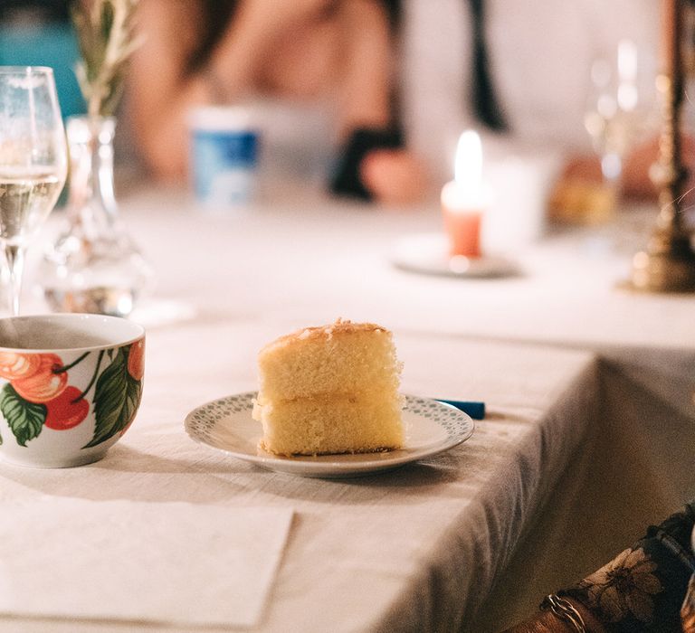 A slice of wedding sponge cake with the bride and groom sitting at their wedding table in the background