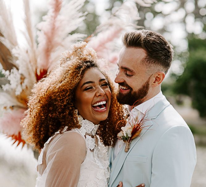 Black bride laughs with groom in pale blue suit