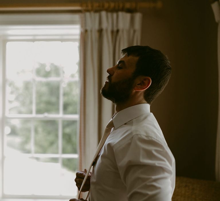 Groom in white shirt straightens tie getting ready for Drenagh Estate wedding