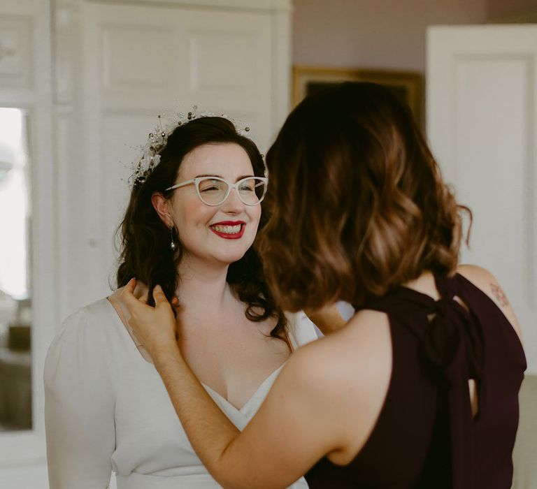 Bridesmaid in navy high neck bridesmaid dress adjusts smiling brides curly hair