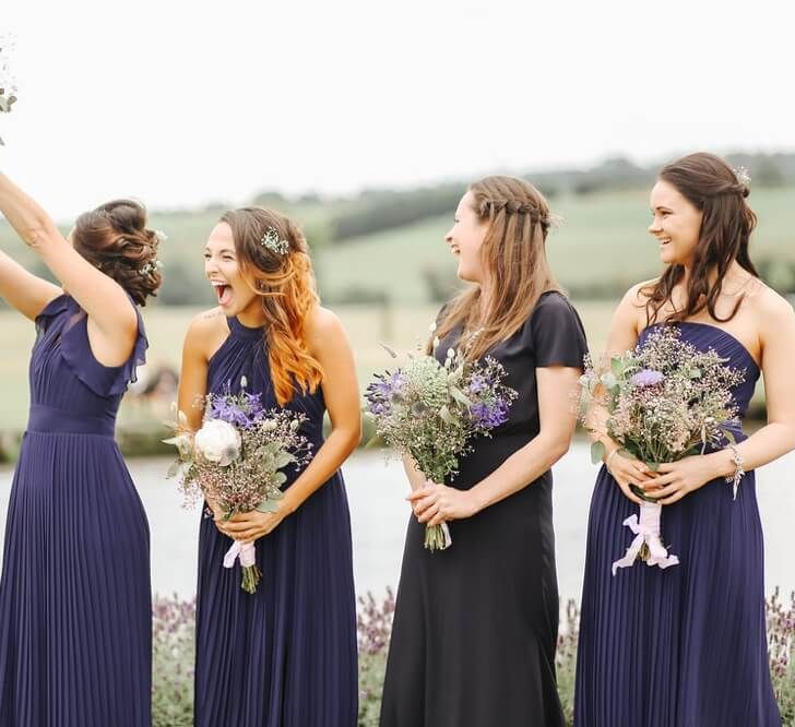 Bridesmaids laughing at an outdoor wedding ceremony wearing assorted pleated navy bridesmaid dresses with long skirts | Belle and Beau Wedding Photography