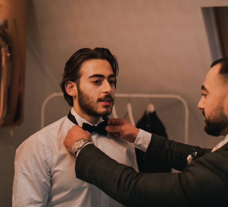 Groom has his bow tie applied by friend on the morning of his wedding