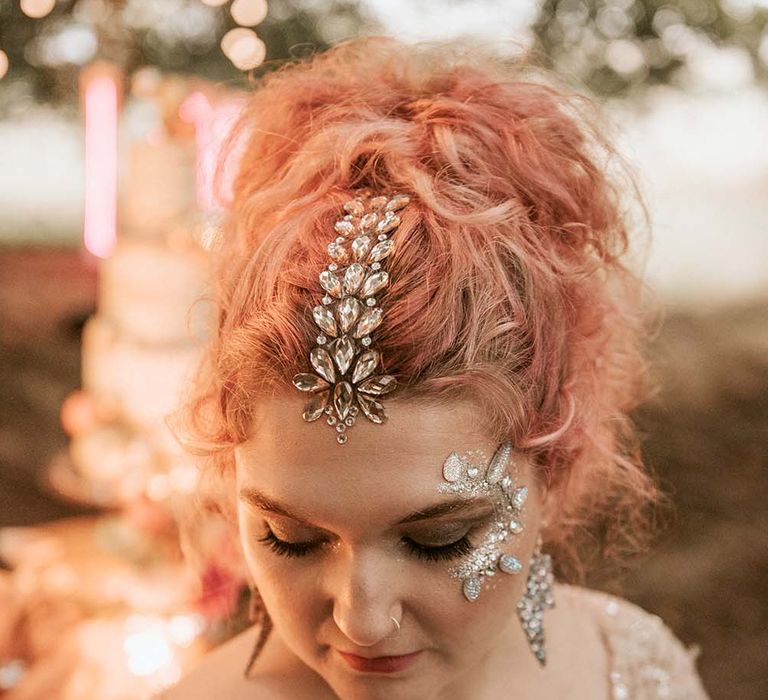 Bride with pink curly hair in gold sequin wedding dress shows off her silver hair gem decoration, face gems and glitter and lightning bolt earrings at festival themed wedding