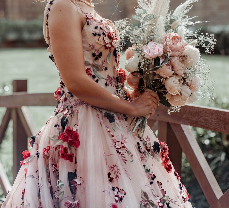 Bride wears floral appliqué wedding gown with blush pink colouring and carries floral bouquet