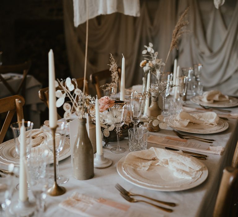 Neutral wedding table decor at modern luxury wedding reception with gold rimmed glasses, ornate tableware, and dried flower centrepiece flowers 