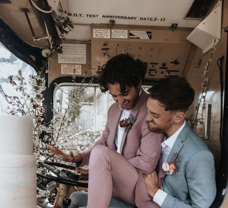 Grooms sit with one another at rustic venue on their wedding day