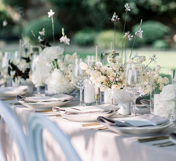 Elegant outdoor tablescape with white tableware, and flower centrepieces 