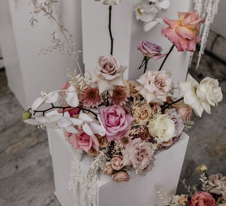 blush pink and white rose and orchid floral arrangement resting on a white plinth 