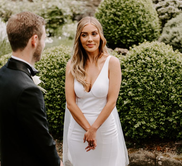 Bride stands looking at groom on her wedding day during wedding ceremony