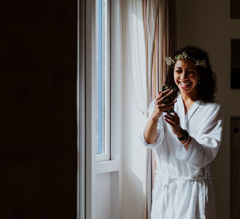 Bride Facetimes on her wedding day whilst showing her makeup and floral crown whilst stood beside open window