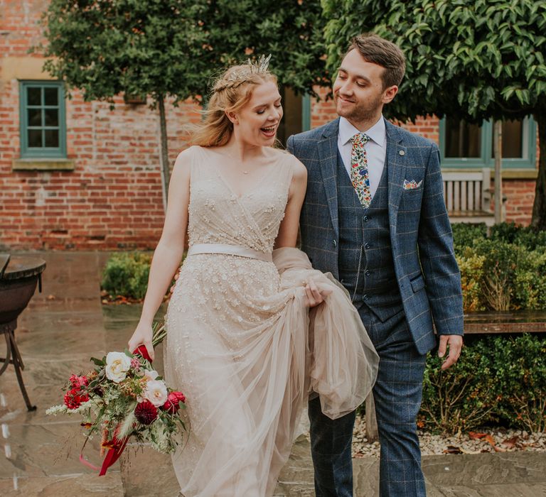 Bride in a tulle and pearl wedding dress and bridal crown laughing with her husband in a grey checked three-piece suit 