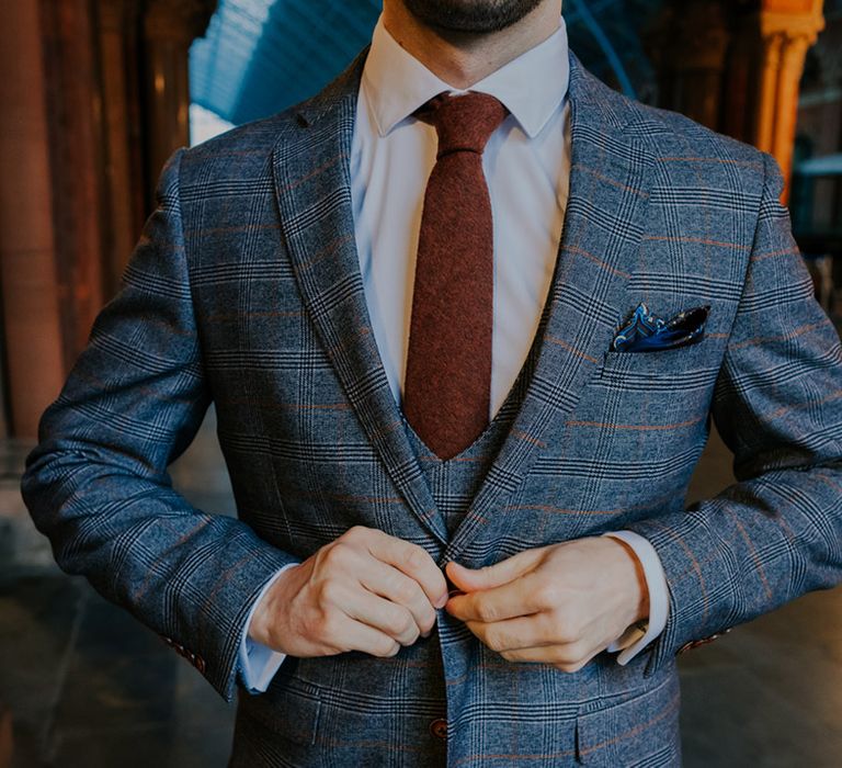 Groom does up his suit as he wears grey jacket with a hint of orange, burgundy tie and silk pocket square