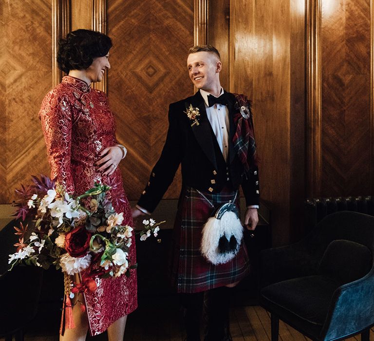 Groom in tartan kilt smiles at bride during town hall wedding