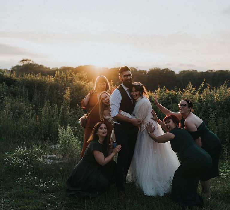 Bride & groom stand with their bridal party as the sun goes down in a field on their wedding day