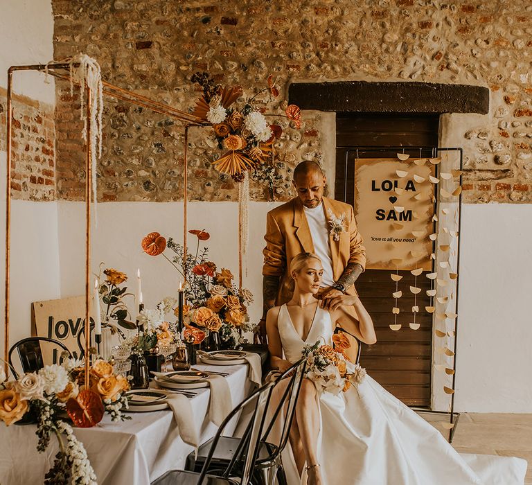 Contemporary wedding inspiration at Curdshall Barn with groom in a mustard suit, orange anthuriums, retro signs and intimate tablescape 