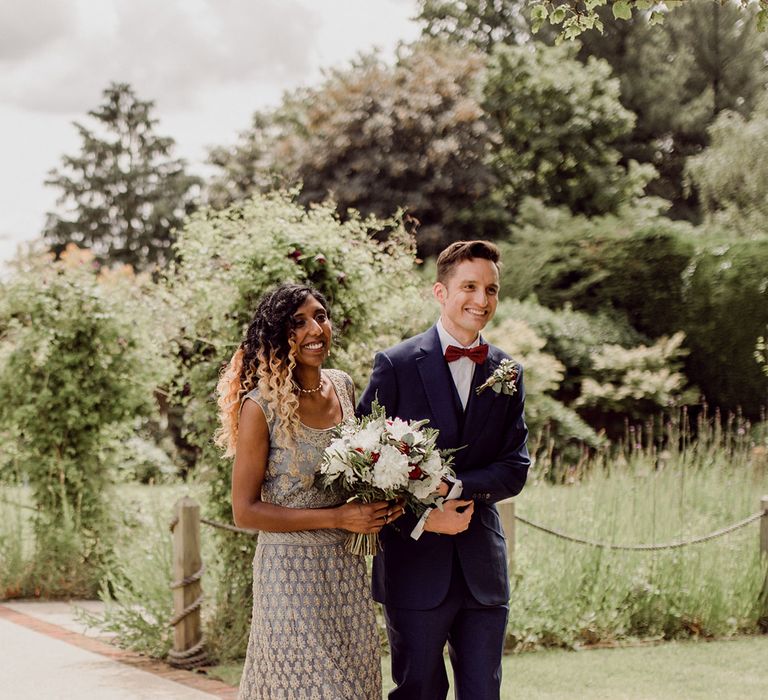 Bride & groom walk together to wedding ceremony as bride holds floral bouquet | Joshua Gooding Photography