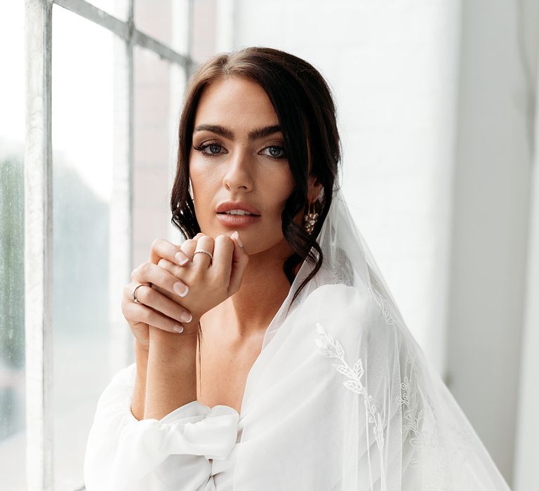 Bride in a long sleeve wedding dress with a loosely pinned up do and an embroidered veil 