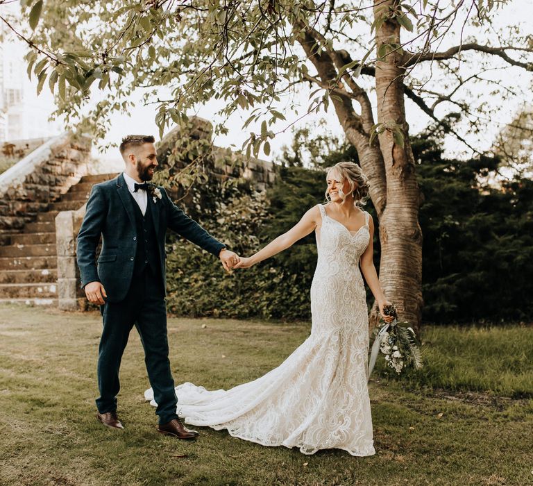 Bride in lace wedding dress holds hands with new husband