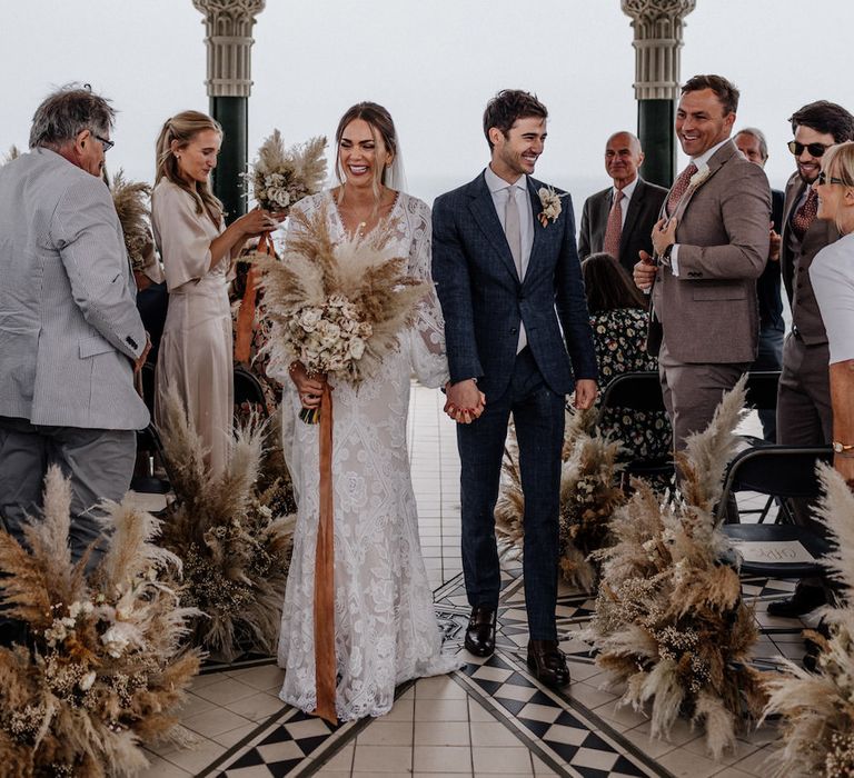 Bride and groom walk up the pampas grass lined aisle