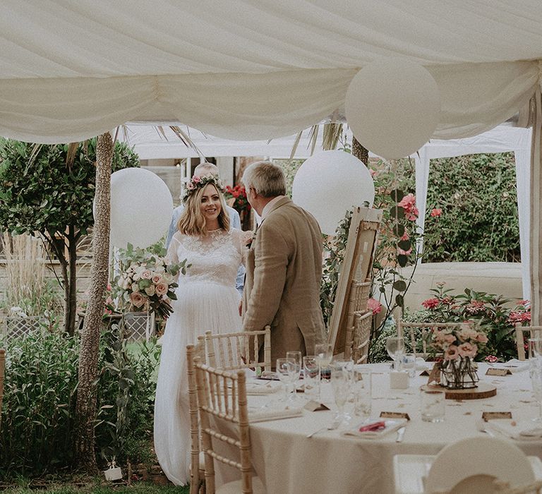 Father of the bride leading his daughter through the back garden marquee wedding reception with white and pink flowers and decor 