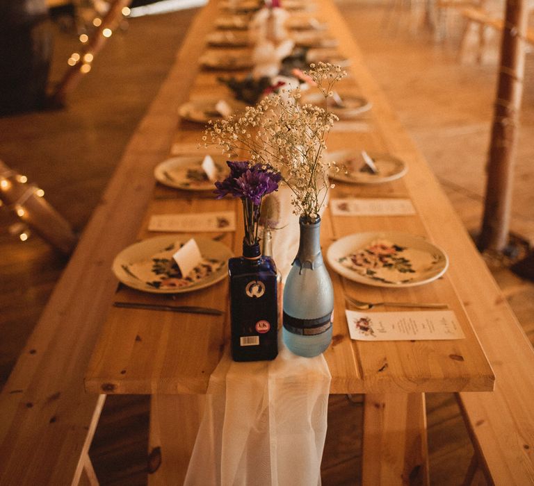 Long wooden table with white table runner, dried flowers in gin bottle and tableware in tipi with fairy lights at Inkersall Grange Farm