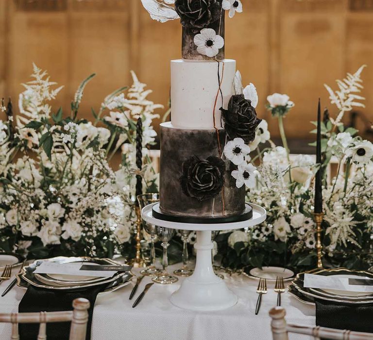 Three-tier wedding cake with black and white tiers on a white cake stand decorated with iced flowers 