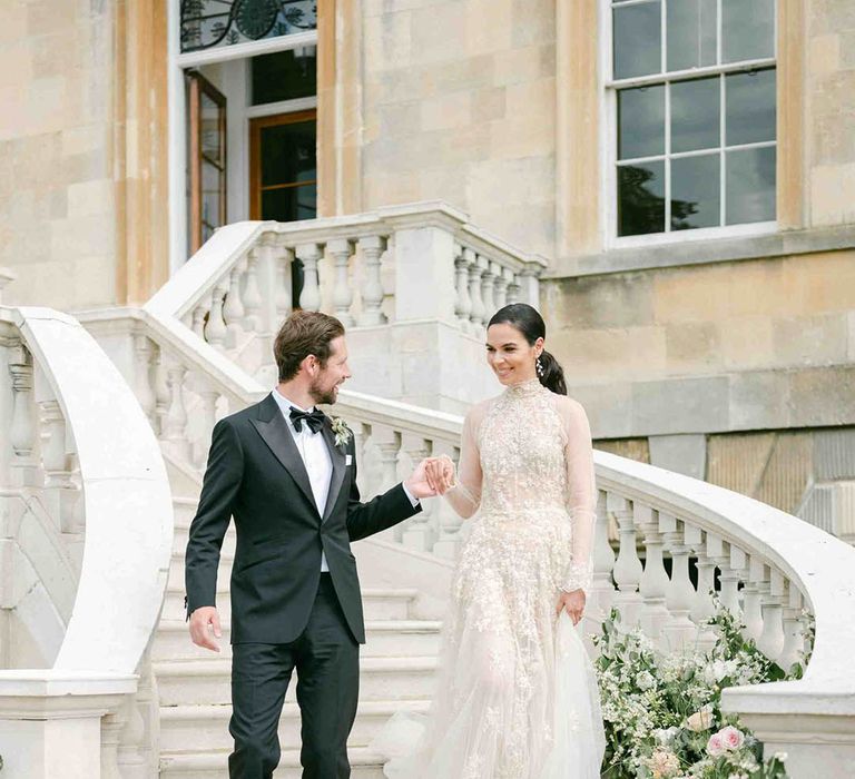 Bride in a romantic lace wedding dress with high neck and long sleeves walking down the stairs at Botley's Mansion with her groom in a tuxedo 