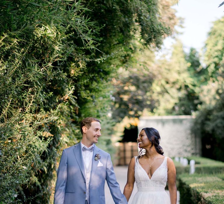 Bride walks with her groom who wears dusty blue suit and white shirt