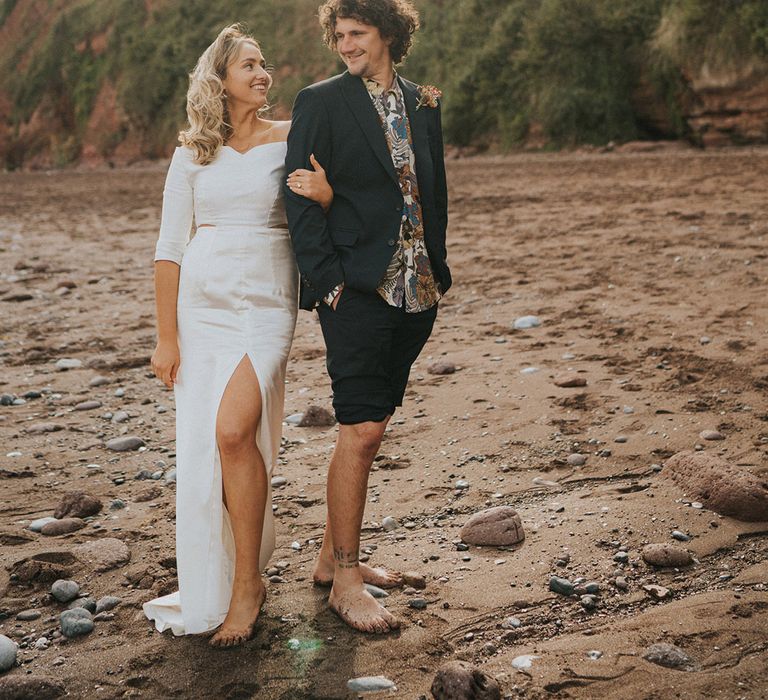 Bride & groom walk along the beach barefoot with one another