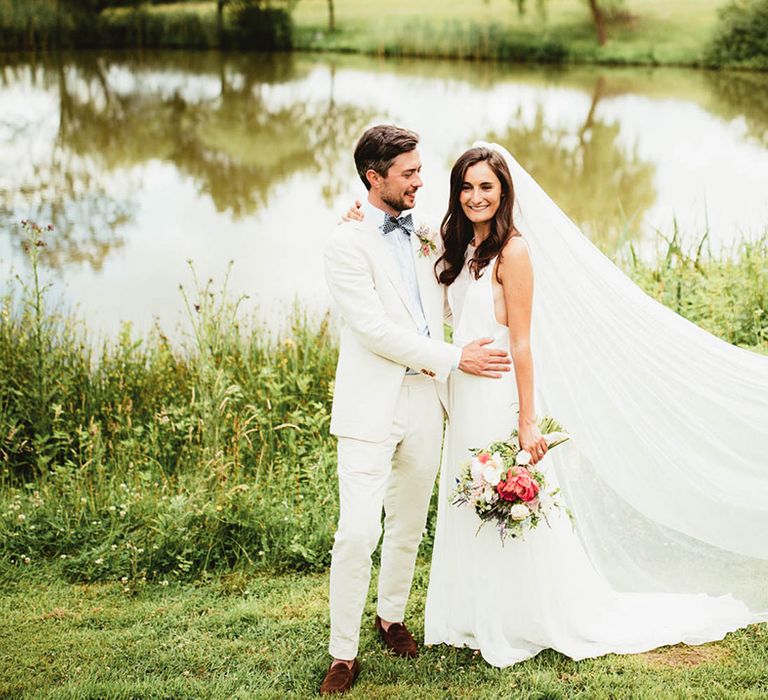 Bride & groom stand outdoors and embrace for couples portraits