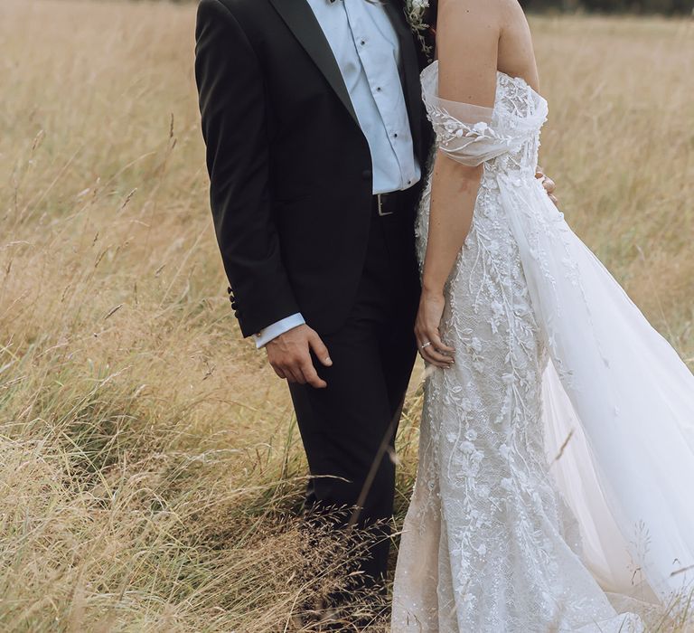 Bride leans into her groom as they stand outside on their wedding day