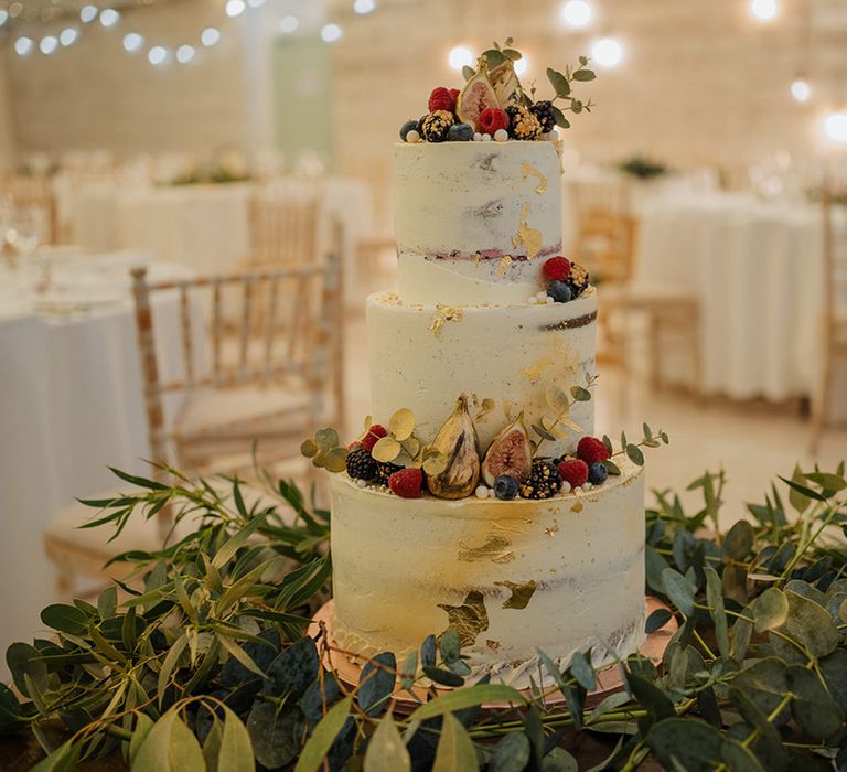 Three tier wedding cake full of fresh fruit and figs surrounded by eucalyptus