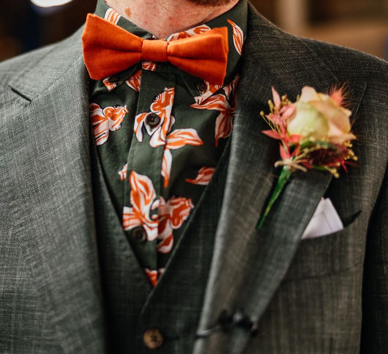 Groom wears light green three piece suit with green and orange patterned shirt and orange bow tie with floral buttonhole