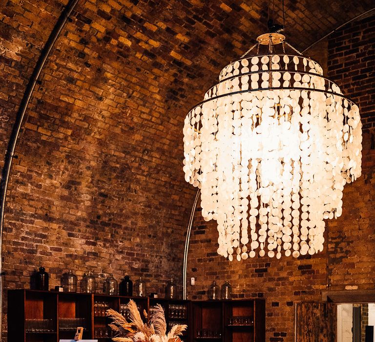 Bar area at 100 Barrington with chandelier, fabric drinks menu, order of the day sign and dried pampas grass and anthurium flowers in a vase 