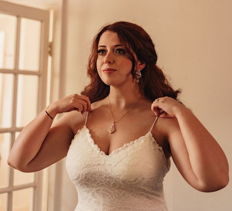 Bride adjusts her Grace Loves Lace wedding gown and wears statement pendant necklace on her wedding day