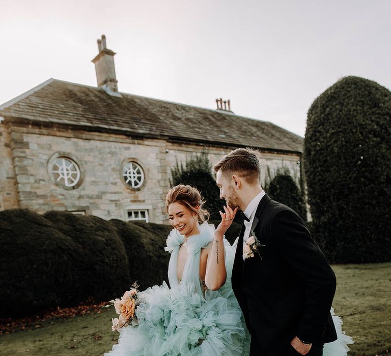 Black tie wedding with groom in a tuxedo and bride in a ruffle light blue wedding dress and bow shoes 