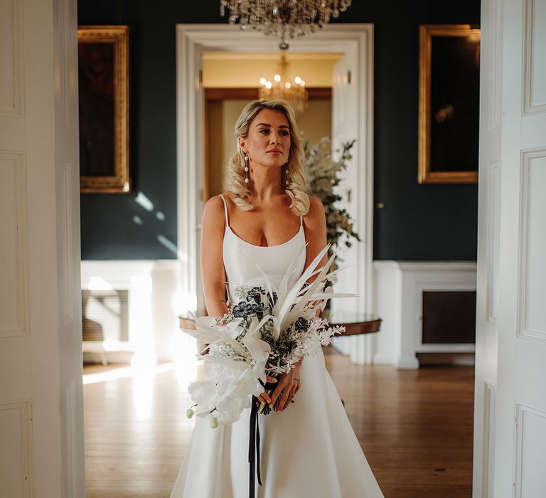 Blonde bride with long wavy hear wearing pearl earrings and holding a dried and fresh flower boqueut with orchids in a princess wedding dress at Hodsock Priory 