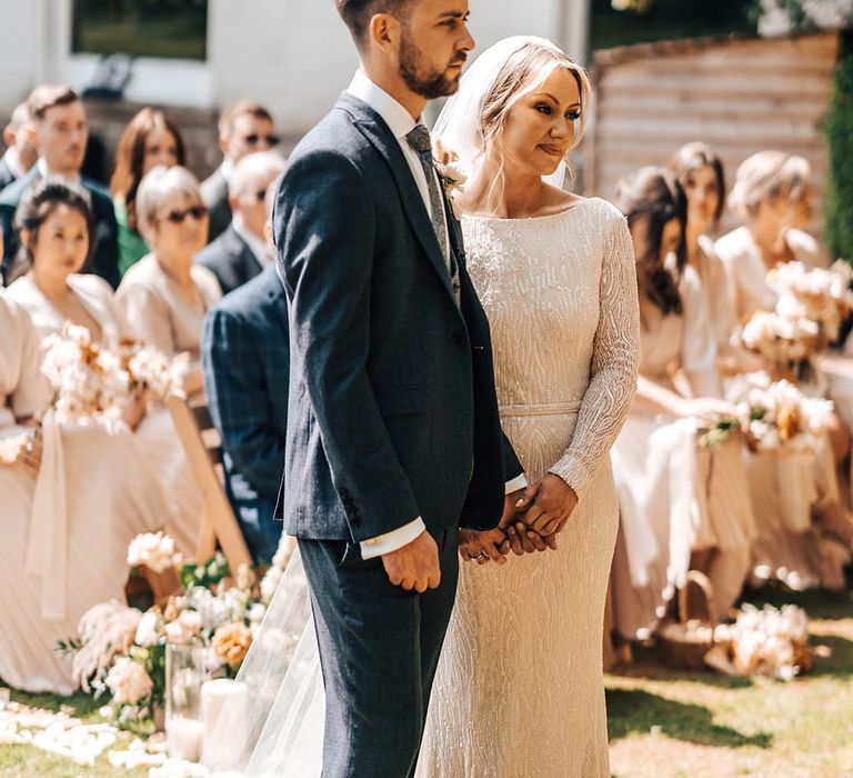 Bride in beaded dress with groom in blue suit smiling together at the altar