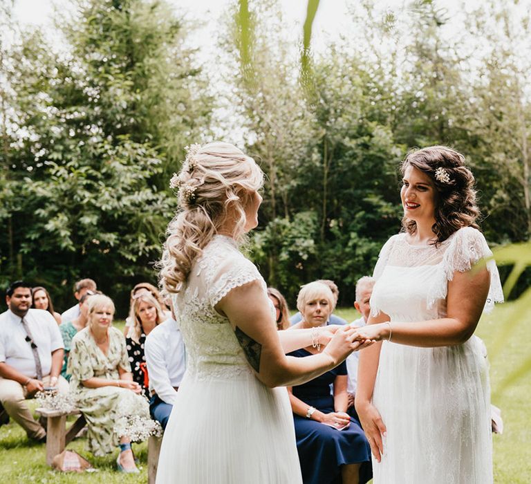 Bride puts the ring on bride's finger at the altar as wedding guests look on during outdoor ceremony