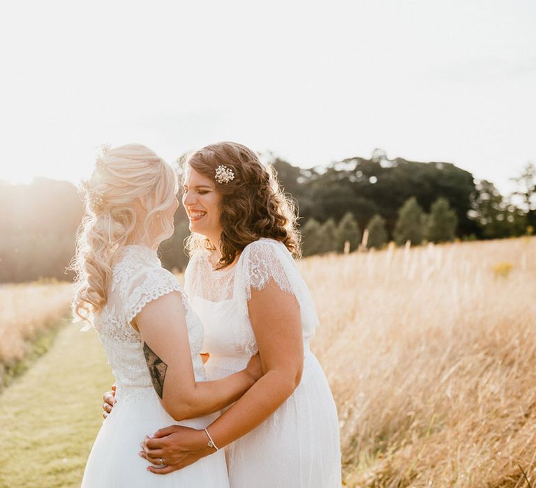 Smiling brides hug each other at golden hour in field 