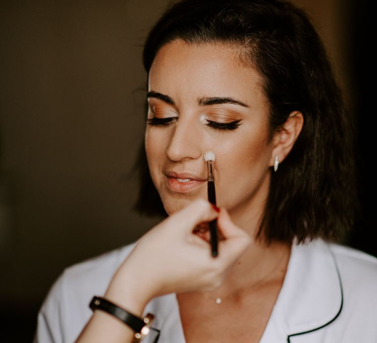 Bride gets her makeup done for her wedding day with glowy and gold tones 