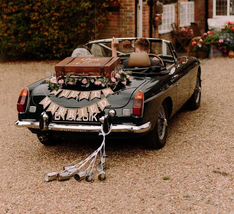 Black convertible car for wedding transport with "just married" bunting and suitcase decoration 