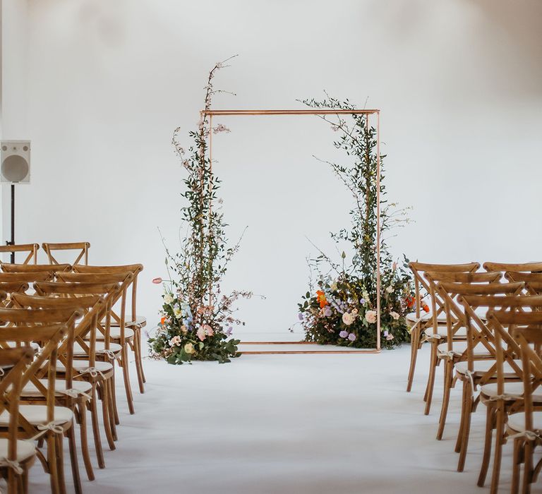 Altar style with copper frame decorated with foliage and colourful spring flowers with wooden chairs