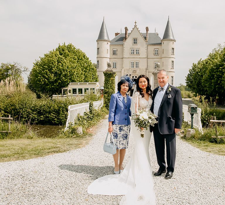 Bride poses in front of the chateau with mother and father in wedding attire for the big day 