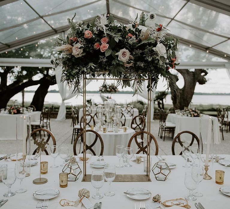 Tall gold table centrepiece with pink and white flowers on white tablecloth with classic and clean styling for outdoor wedding 