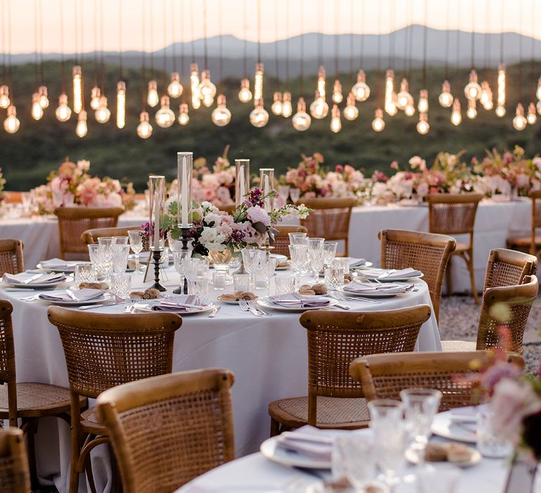 Outdoor wedding ceremony in Tuscany complete with decorative Edison bulbs chandelier along head table 