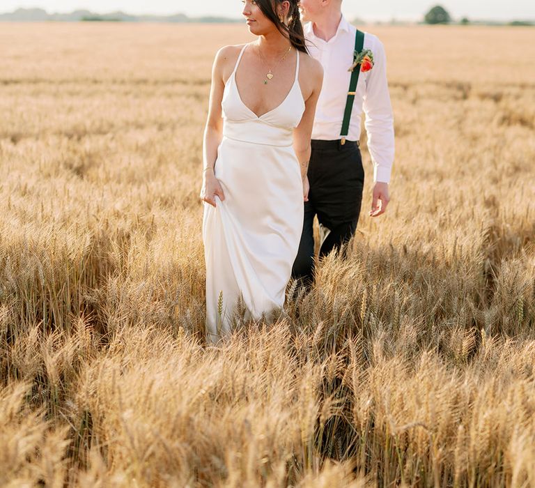 Bride & groom walk through golden fields as bride wears homemade silk satin gown and gold necklaces 