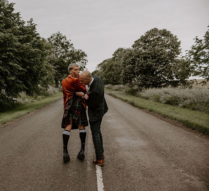 Groom cheekily lifts kilt of his groom outdoors as they walk through the street on their wedding day