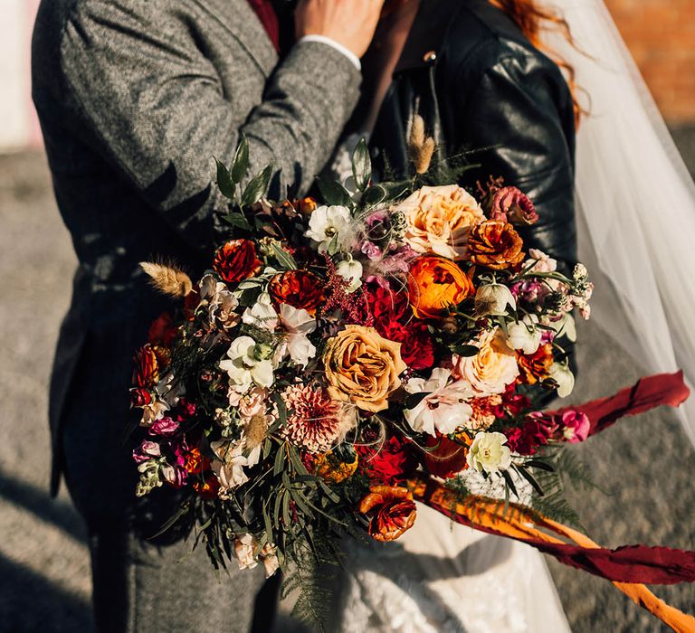 Groom in grey suit with bride in a leather jacket cover-up as they kiss 