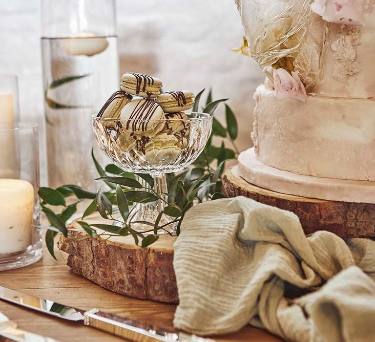 Dessert table with macaroons in a glass dish on a rustic tree slice 